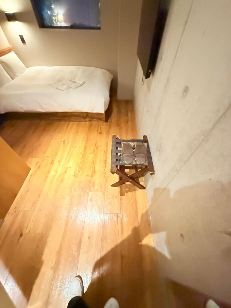 객실 벽면과 침대 사이에 놓인 접이식 캐리어 받침대